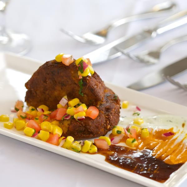 Two Passage to India Indian fritters topped with corn and tomato salsa, with sauces on a white plate.