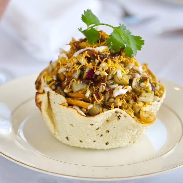 Indian Bhel Puri chaat, a savory snack, served in a crispy papadum bowl on a white plate.