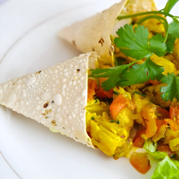 Two Indian papadum wraps filled with yellow curry, red peppers, and fresh cilantro on a white plate.