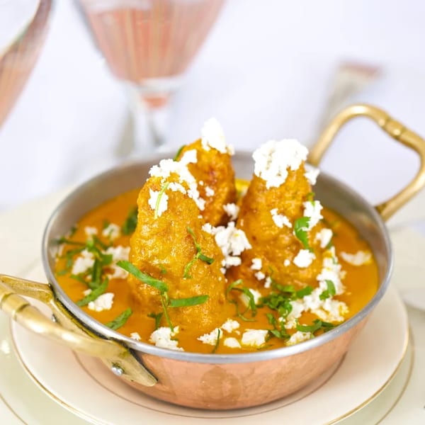 Passage to India's Malai Kofta, golden dumplings in creamy orange sauce, topped with crumbled paneer and herbs.