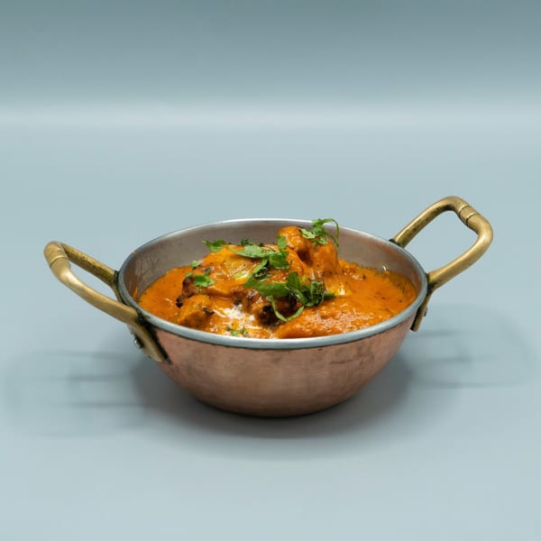 Indian butter chicken in a copper serving bowl, garnished with fresh cilantro.