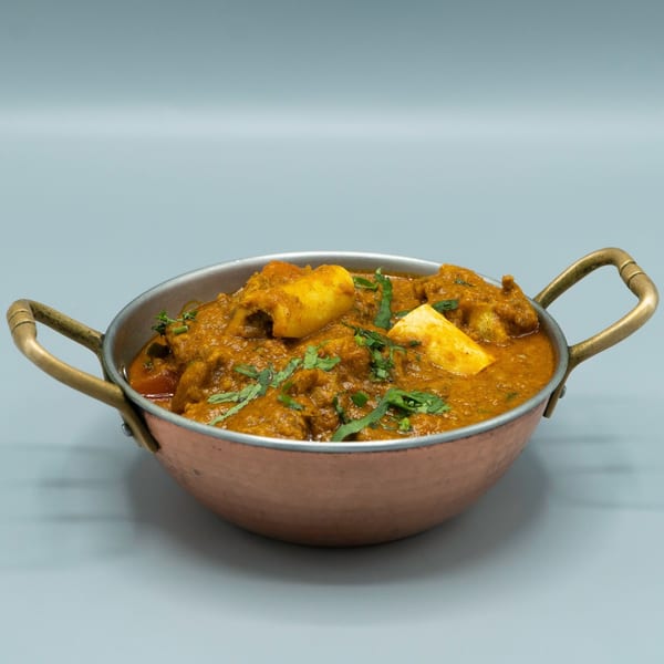Passage to India's chicken curry with paneer and cilantro in a copper serving bowl.
