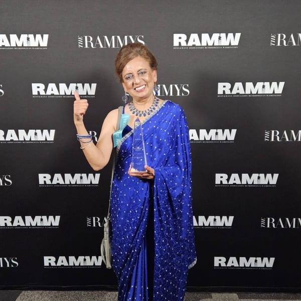 A smiling woman in a blue sari holds an award and gives a thumbs-up at The RAMMYS event.