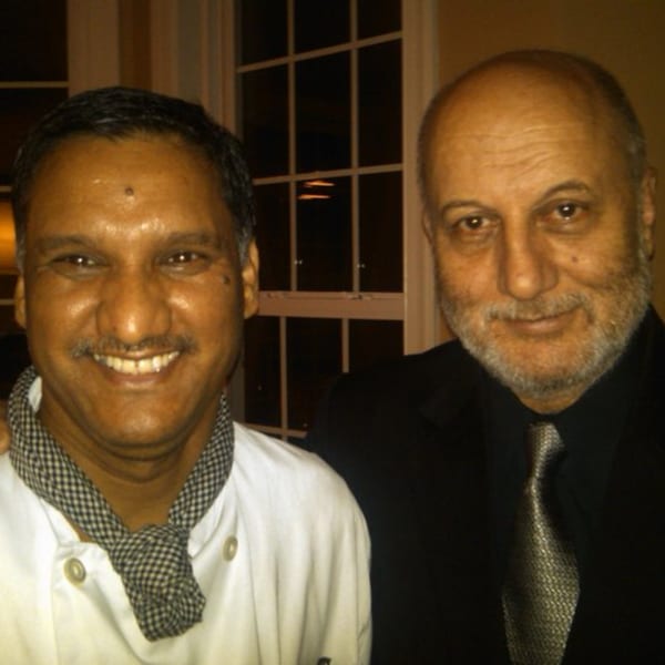 Two men, one in a chef's coat and the other in a suit, smiling at the camera.