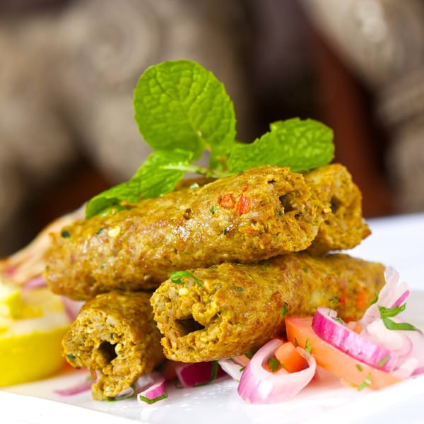 Passage to India's seekh kebabs, garnished with mint, red onions, and lemon wedges.