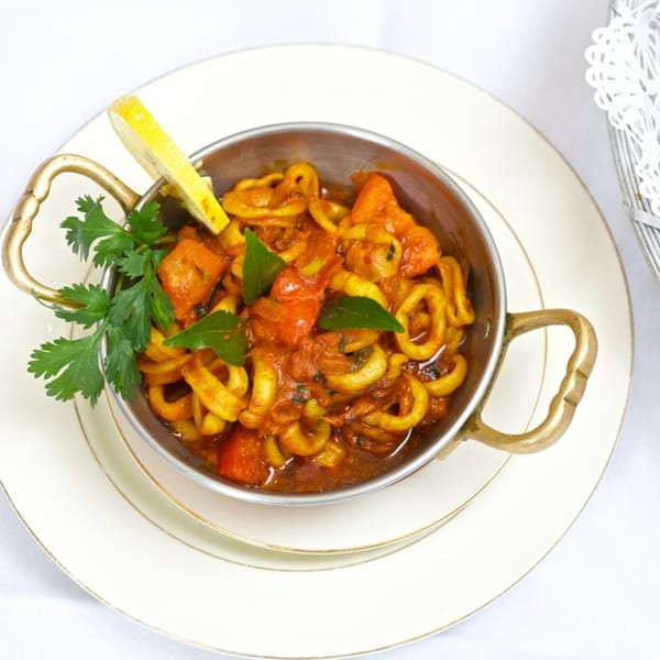 Indian calamari curry in a brass bowl, garnished with cilantro and a lemon wedge.