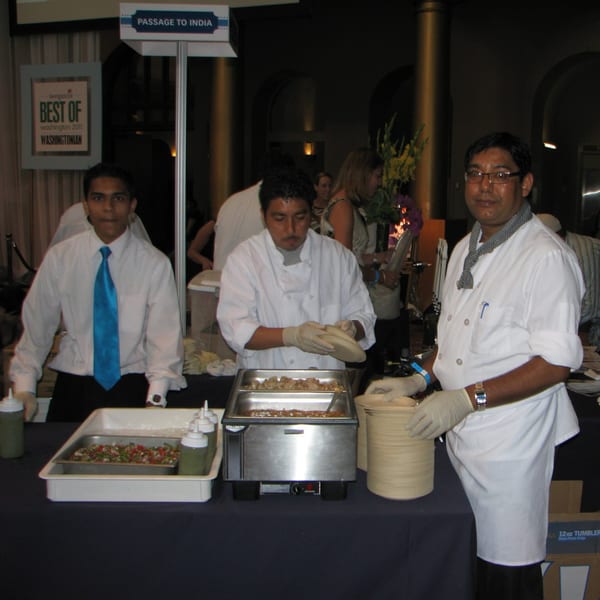 Three Passage to India staff members serving Indian food at a buffet station.