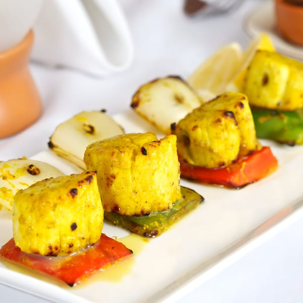 Grilled paneer and vegetables on a white plate, with lemon wedges and a white napkin in the background.