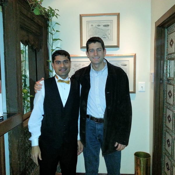Two men, one in a vest and bow tie, the other in a jacket and jeans, smiling.